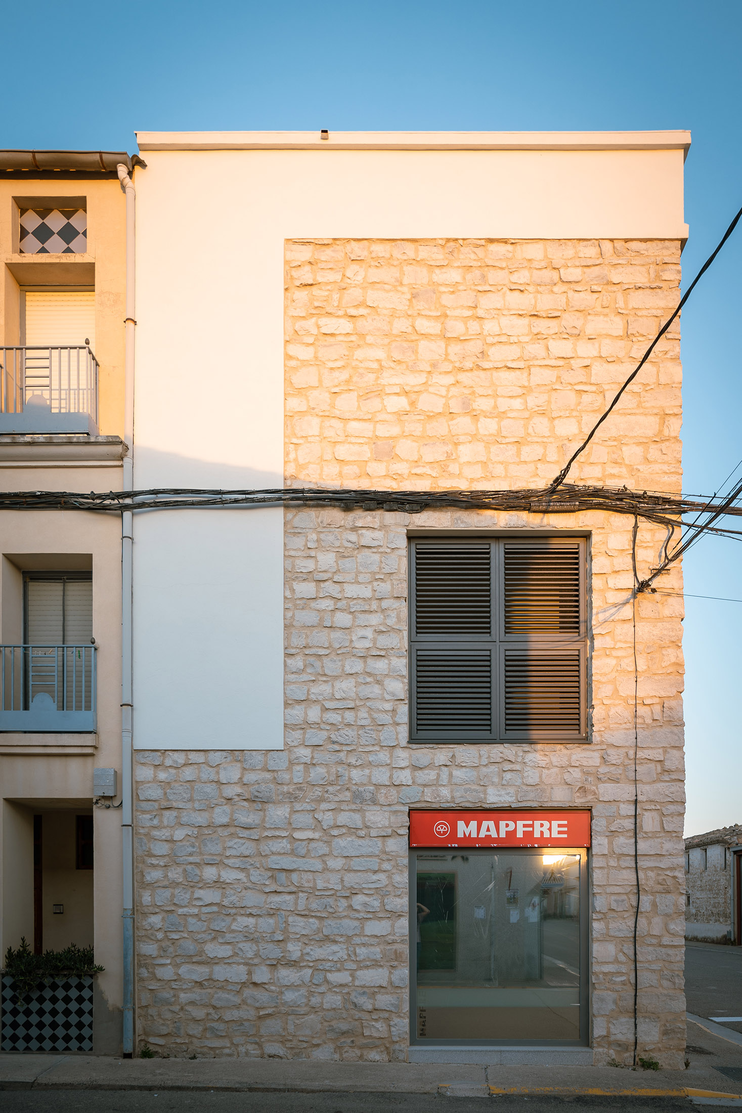 Composición de fachada combinando paños de piedra y enfoscado blanco, con un gran ventanal y rótulo